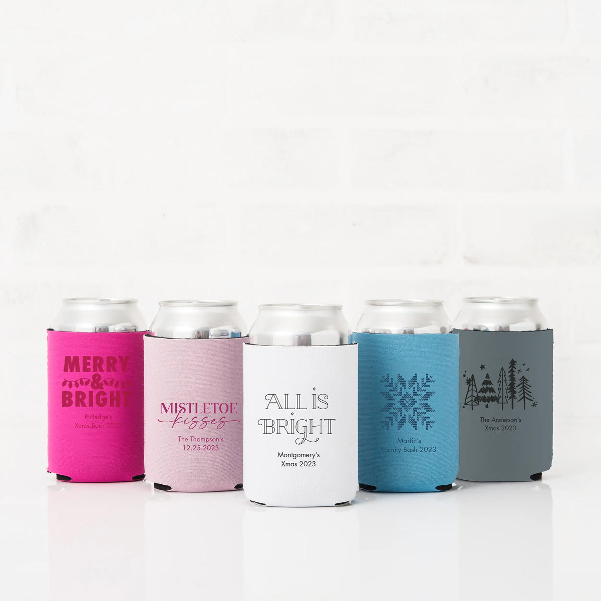 Five personalized Christmas koozies in hot pink, blush, white, blue, and gray with Merry and Bright, Mistletoe Kisses, and family holiday bash designs on cans
