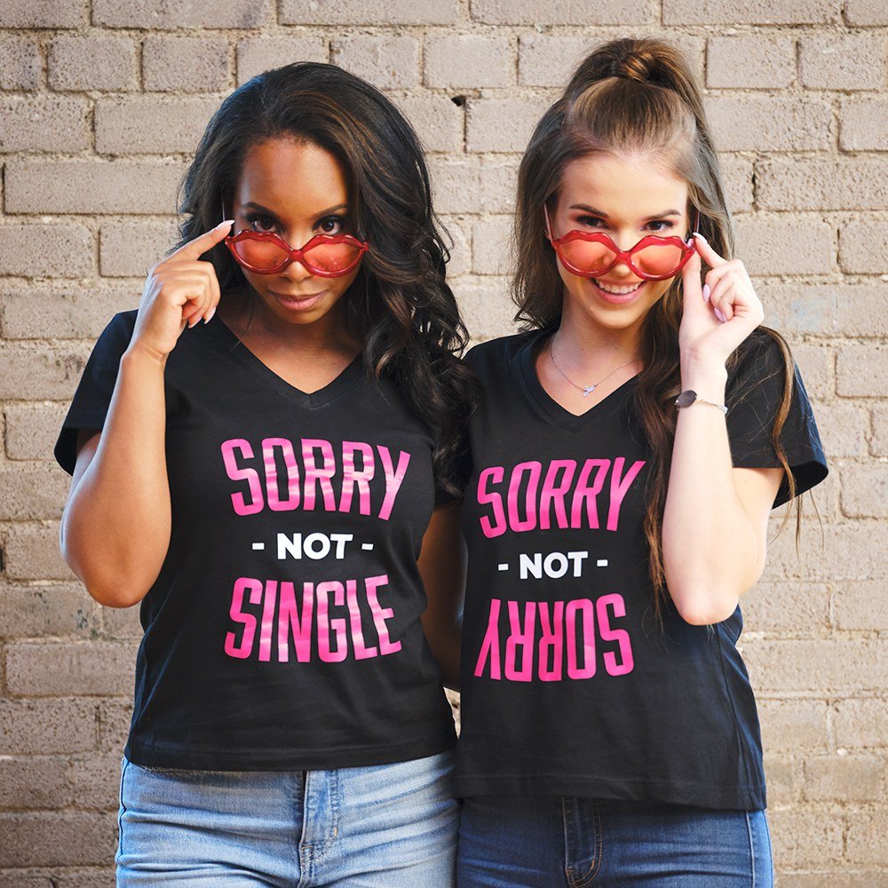 Two friends in matching black Sorry Not Single shirts wearing red lip-shaped bachelorette party sunglasses from Forever Wedding Favors